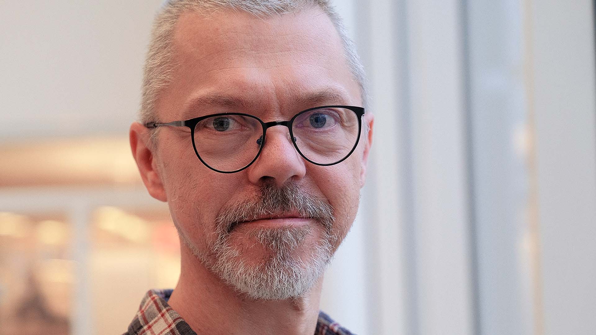 Porträttfoto regissören Pelle Öhlund. Vitt kort hår, ljusgrått kort skägg och svarta glasögon. 