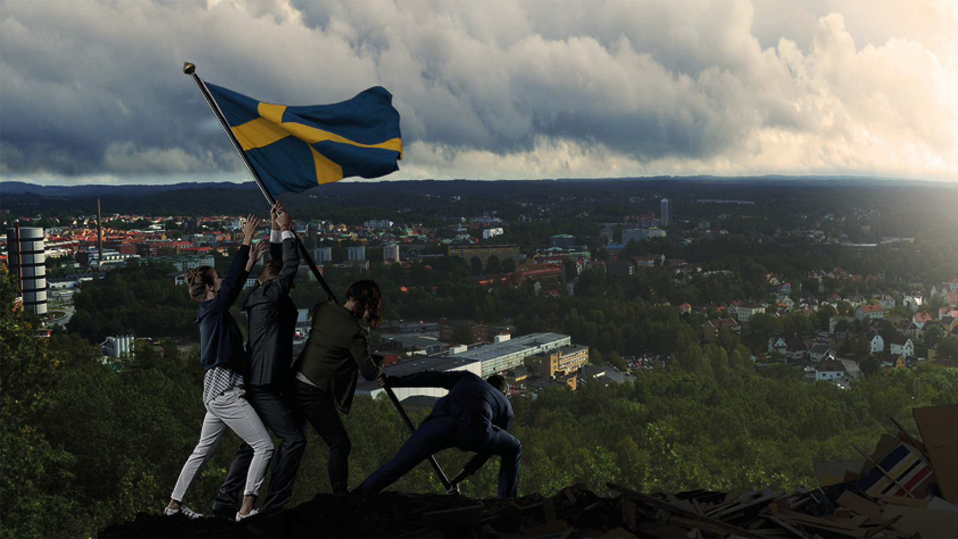 4 personer reser en svensk flagga tillsammans  på en höjd med utsikt över Borås. 