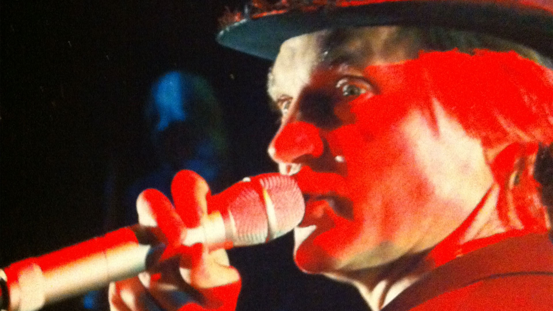 Närbild av skådespelaren Lennart Eriksson hållande i en mikrofon i starkt rött ljus.