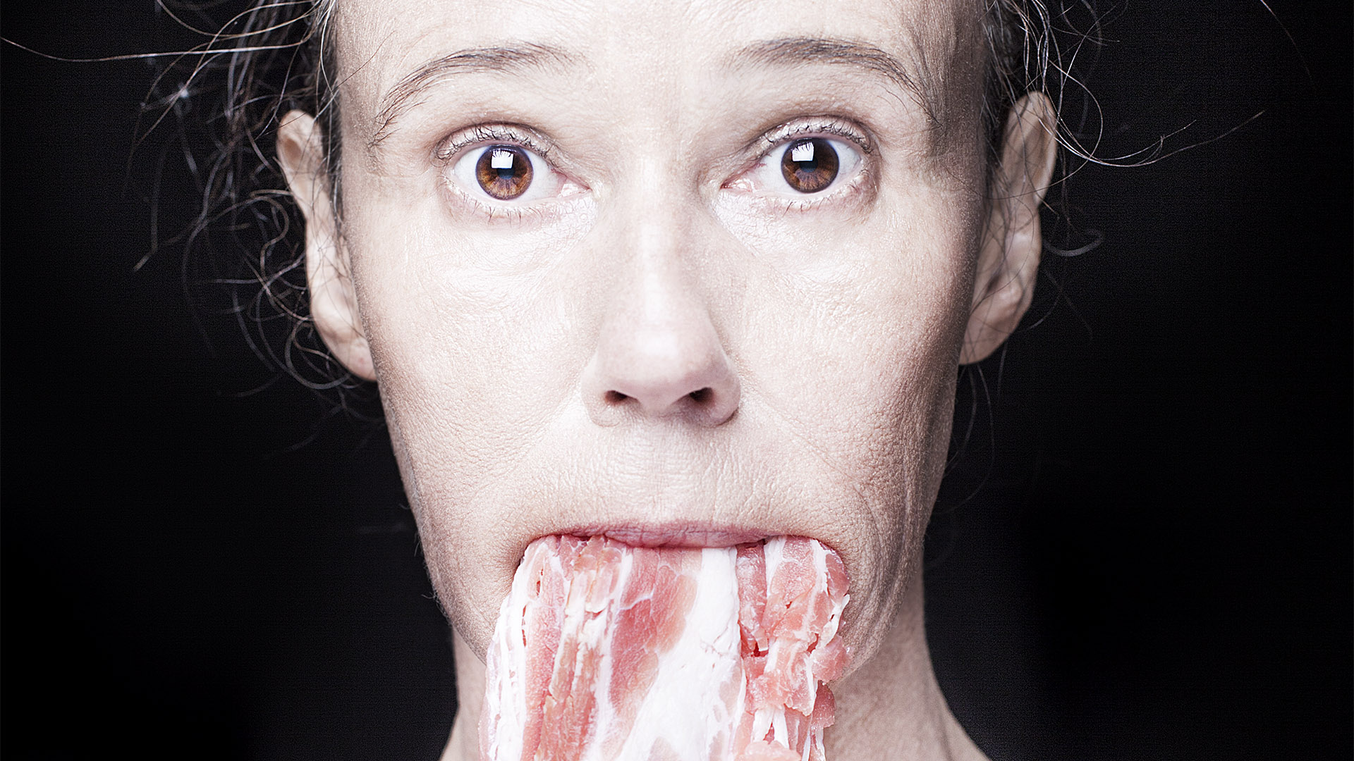 Närbild på en kvinna med råa bacon hängande ut ur munnen.
