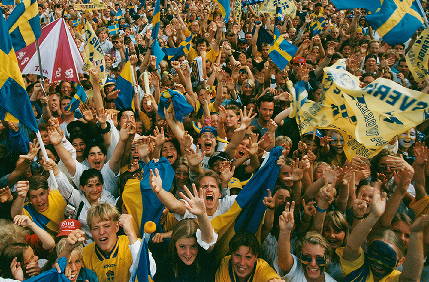 Klickbar bild Den varmaste sommaren. En glad folkmassa som sträcker sig mot kameran i ett jubel. I folkhavet syns många svenska flaggor.